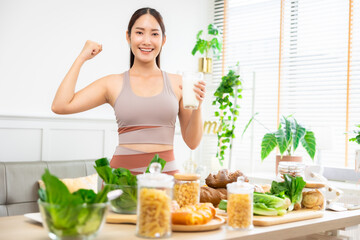 Attractive fitness asian woman finishing workout and drinking protein milk shake vitamins and vegetable after training at home. Bodybuilding. Healthy lifestyle.