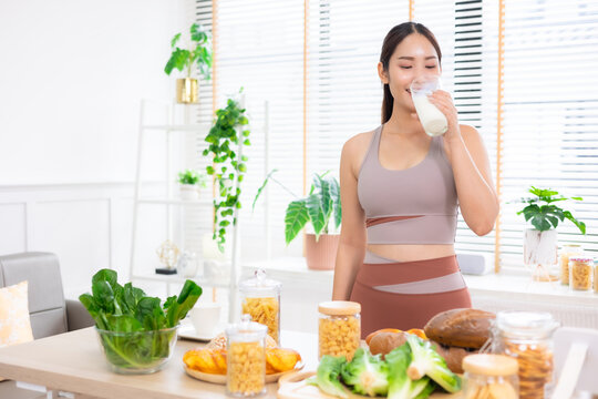 Attractive fitness asian woman finishing workout and drinking protein milk shake vitamins and vegetable after training at home. Bodybuilding. Healthy lifestyle.