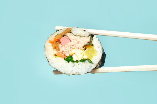 Wooden chopsticks with korean kimbap roll on blue background close-up.