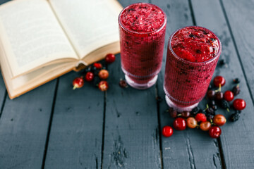 Two vibrant mixed berry smoothies in textured glasses on a dark wooden table, surrounded by fresh...