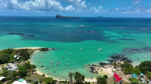 Cap Malheureux, Mauritius: Aerial footage showing the vibrant red rooftop of Notre Dame Auxiliatrice church beside turquoise waters dotted with boats, with Gunner&rsquo;s Quoin (Coin de Mire) rising on the 
