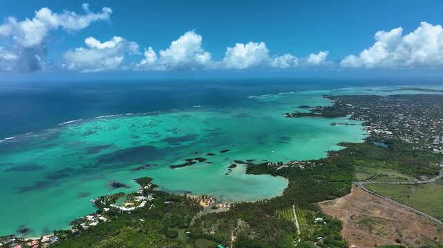 Sweeping aerial footage over the turquoise lagoon and lush northern coastline of Cap Malheureux, Mauritius, revealing coral patches, quiet beaches, and residential areas bordering the Indian Ocean