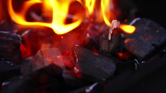 Burning coals glowing red with bright yellow flames in close-up firepit view