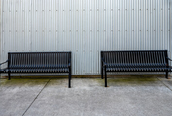 Background of Twin Shining Black Metal Benches Against a Silver Metal Wall.