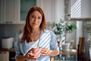 Smiling woman drinking coffee at home and looking at camera.
