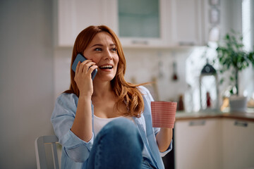 Happy woman talking over cell phone while drinking coffee at home.