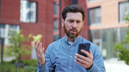 Frustrated businessman feeling stressed reading bad news on his phone while standing outdoors. He's dressed in casual clothes, and experiencing disappointment and shock. - Powered by Adobe