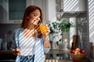 Happy woman drinking orange juice in kitchen.