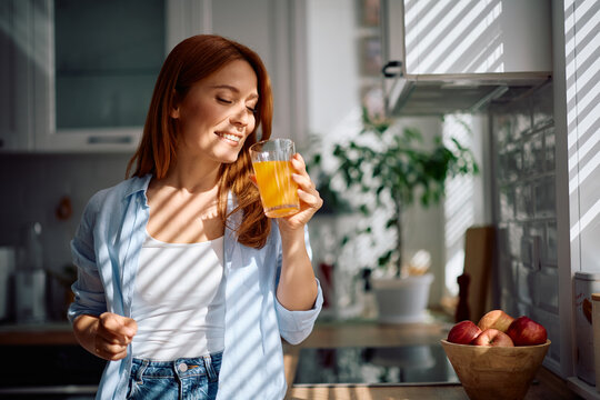 Happy woman drinking orange juice in kitchen.