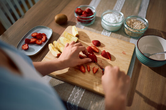 Close up of woman cutting strawberries and apples while making fruit oatmeal.
