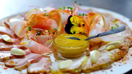 mint plates of white and black color with boiled pork, slices of lard, herbs with a bottle of cognac, a buffet, with mustard and red sauce on a table with a beautiful tablecloth.