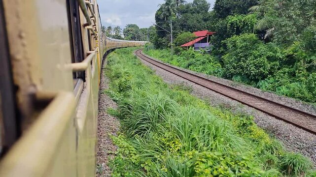 A cinematic shot of indian train speeding on the curvy track amidst amazing nature with cloudy sky