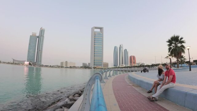 Abu dhabi, UAE - 25th april, 2025: sunset timelapse couple visitors enjoy relaxed moment sit on bench enjoy sunset by Etihad Towers in Abu Dhabi, architecture with public space and modern city life
