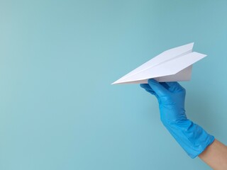 Girl's hand in blue rubber protective glove holds white paper airplane on blue background