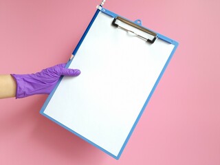 Girl's hand in purple protective glove holds tablet with blank white sheet of paper on pink background. Space for text 