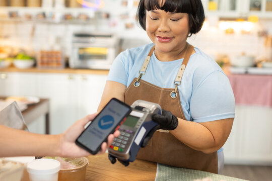 Small business owners are selling .Handsome young caucasian waiter servicing the customer with swiping machine in a cafe. Cashless contactless payment with credit debit card. E-banking .