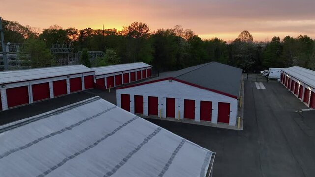 Aerial flyover rental self-storage units and green forest landscape in scenic area of american town. Golden sunset with pink clouds in USA. Rising drone revealing shot.