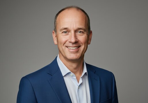 Portrait of a smiling mature businessman in a blue suit and light blue shirt against a solid gray background