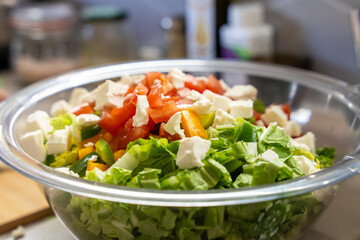 Glass bowl filled with fresh vegetable salad topped with diced tomatoes and white cheese, highlighting clean eating and healthy lifestyle concept