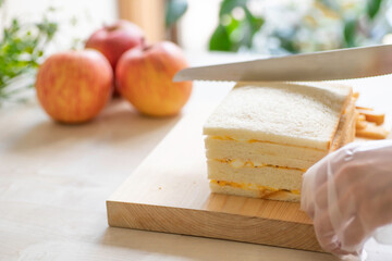 明るいキッチンでサンドイッチをカットする朝