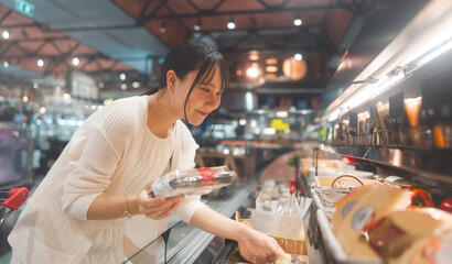 Young adult asian woman consumer choosing cheese dairy products at supermarket store buying food