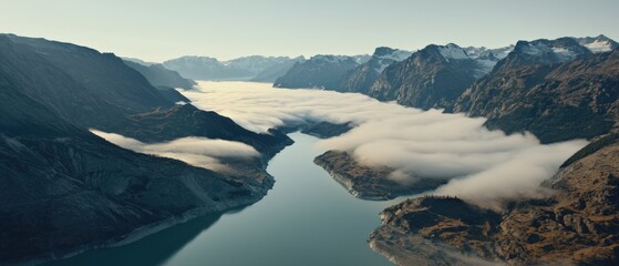 A deep blue river meanders through a mountainous landscape, with snow-capped peaks and a hazy blue sky.
