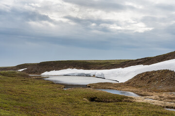 A small pond in the highlands of the Varangerhalvøya National park with lingering snow Northern Norway