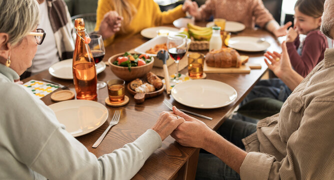 Family enjoying a warm and joyful gathering at home during the weekend, sharing a meal and holding hands around the table.