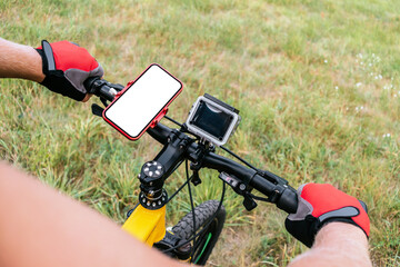 Close-up mockup of a smartphone on the handlebars of a bicycle. Background on meadows with green...