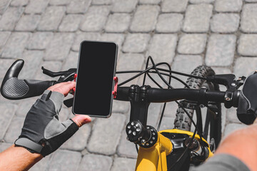Top view. Close-up of a black mobile phone screen on the handlebars of a bicycle. Background of sidewalk tiles of gray color.
