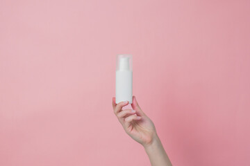 White unbranded cream bottle with pump in hand on pink background. Concept of beauty. Product cosmetic advertising