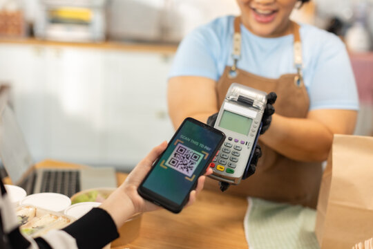 Small business owners are selling .Handsome young caucasian waiter servicing the customer with swiping machine in a cafe. Cashless contactless payment with credit debit card. E-banking .