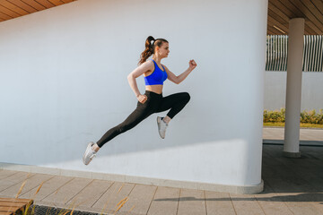 A woman energetically leaps in the air, exhibiting grace and strength against a clean, white...