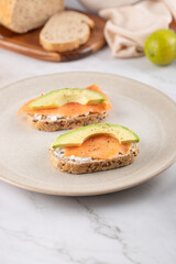 Two whole grain seed toasts with avocado and smoked salmon on cream cheese. Concept of healthy breakfast with fresh ingredients and soft natural light