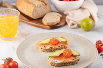 Multigrain toast with salmon, avocado and tomato served with orange juice, bread and fresh vegetables. Concept of healthy breakfast and modern lifestyle
