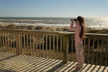 Side view young girl binnoculars on deck at ocean Outer Banks