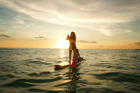 Teen girl paddle boarding with younger sister at sunset Gulf of