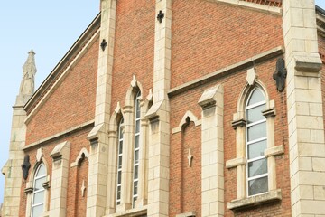 Neo Gothic Revival church facade with red brick walls and light stone trim featuring pointed arch lancet windows decorative buttresses and tracery under an overcast sky