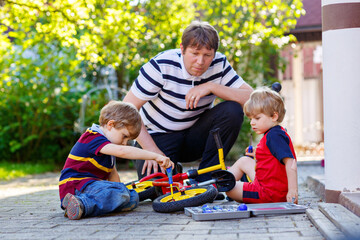 Two happy little kid boys and father repair chain on bikes and change wheel of balance bicycle