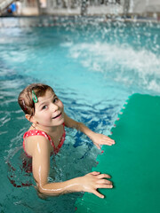 Little girl having fun in indoor swimming pool. Happy child swimming and splashing with water....