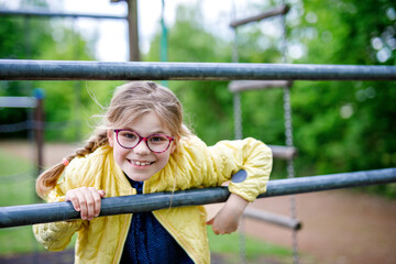 Obraz premium Little girl doing gymnastics on a climbing frame, horizontal bar on school yard. Child enjoying school break.