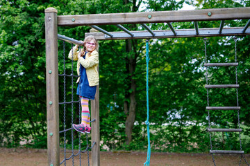 Little girl doing gymnastics on a climbing frame, horizontal bar on school yard. Child enjoying...