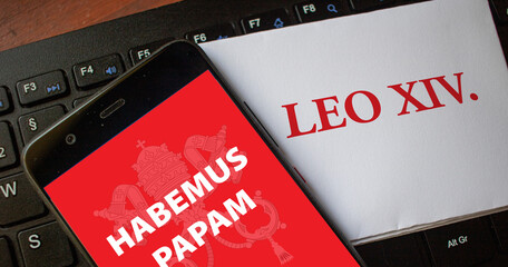 Fototapeta na wymiar The words habemus papam on a smartphone with the name Leo XIV as the new pope on a piece of paper lying on a keyboard