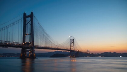 Fototapeta premium Sunset over the majestic Akashi Kaikyo Bridge, a symbol of engineering marvel and connecting pathways. The tranquil waters reflect the vibrant sky creating a stunning image.