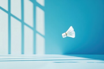 A white badminton shuttlecock floats in the air against a blue wall with window light shadows falling