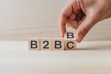 Hand arranging wooden blocks spelling B2B or B2C, showcasing business strategy and market choices, symbolizing decision-making and flexibility in a business context