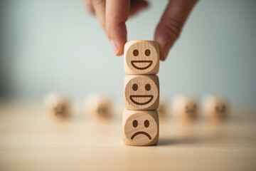 Wooden cubes with happy and sad faces stacked, hand placing top cube, representing customer feedback or satisfaction levels