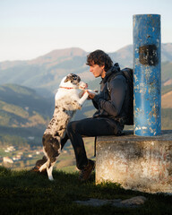 Young hiker interacting with his border collie while resting on a mountain top in aiaraldea, basque...