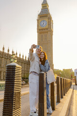 A joyful couple takes a playful selfie in front of Big Ben, capturing the essence of their London visit. The warm sunlight enhances the romantic atmosphere of their cherished moment
