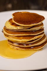 pancakes and bee honey on a white bowl, a tower of small milk pancakes on a ceramic bowl with bee honey